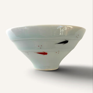 A white ceramic bowl with hand-painted fish motifs in black and red, set against a plain off-white background.