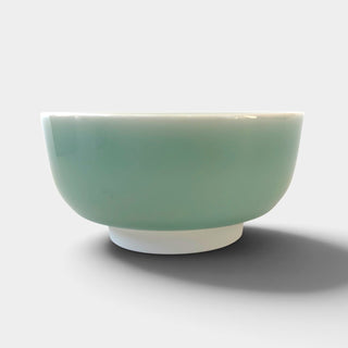 A ceramic bowl with a pale celadon green exterior and a white interior.
