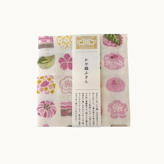 A folded Japanese cotton napkin with a traditional floral and fruit pattern, wrapped with a white paper band featuring Japanese text.