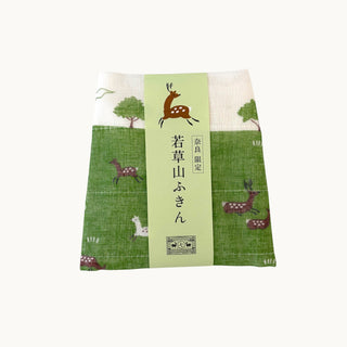 A square fabric cloth with a green grassy field and deer pattern, wrapped in a light green paper band with Japanese text and a deer illustration, shown on a plain white background.