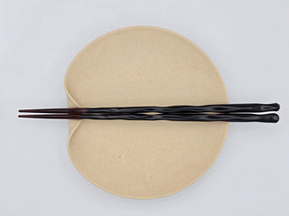 Toki Meki Workshop black and red lacquered wood chopsticks on a speckled beige plate. Dishwasher safe, made in Japan.